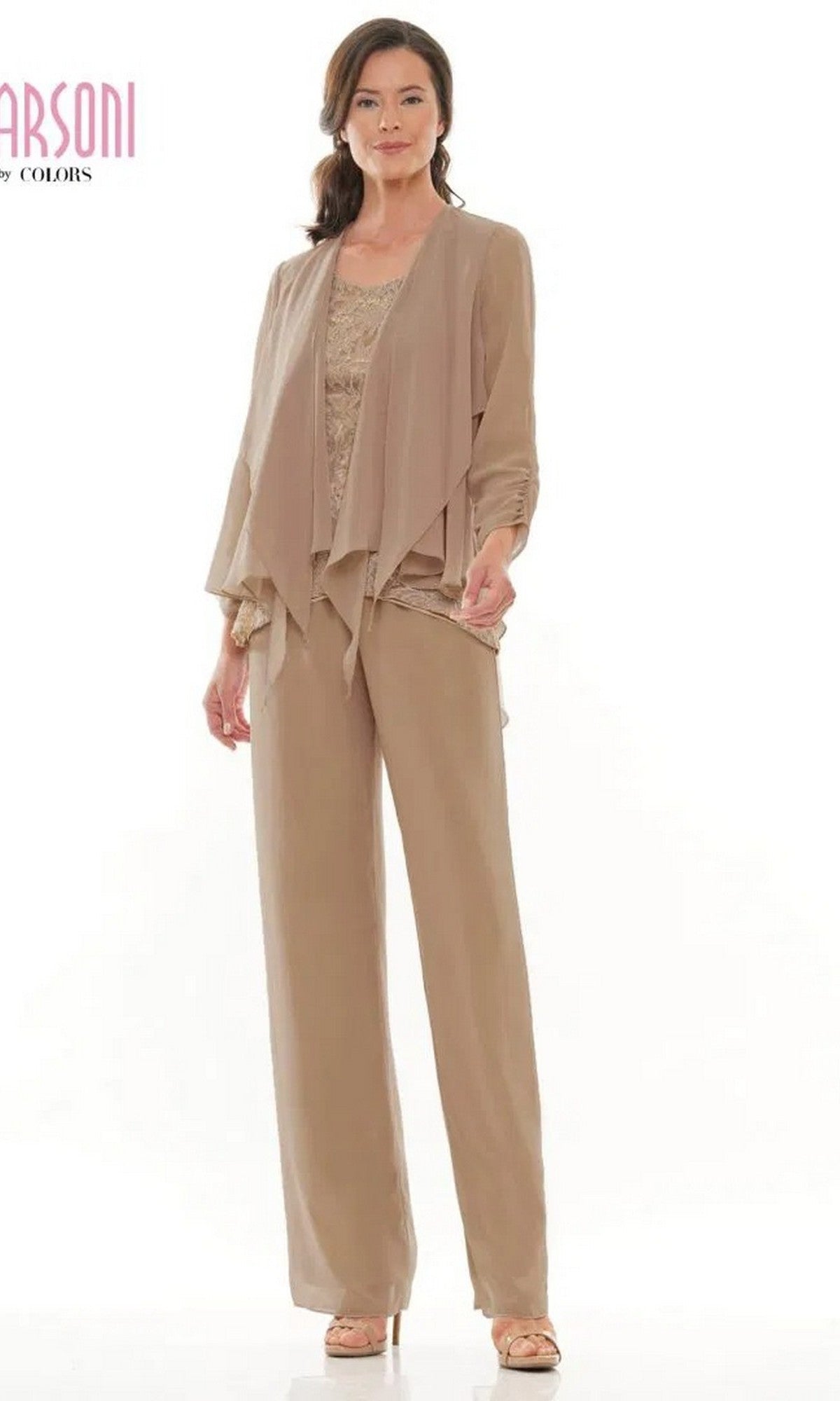 A woman stands wearing the Marsoni M303 Long Formal Pantsuit in Bermuda Sand, featuring a light brown chiffon jacket over a sleeveless lace top, with matching wide-leg pants and open-toe shoes.